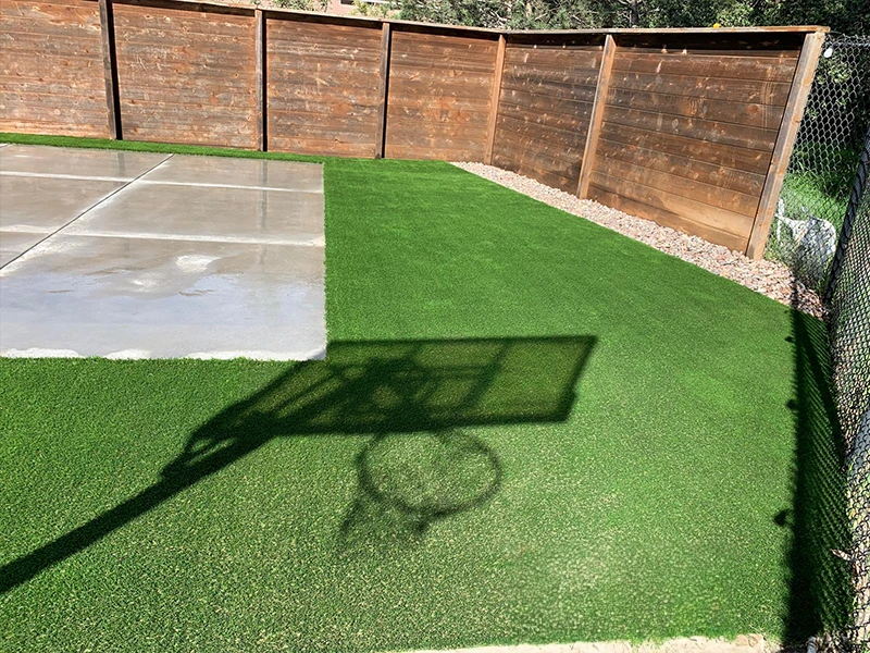 Basketball hoop and court on green turf, with a wooden fence in the background