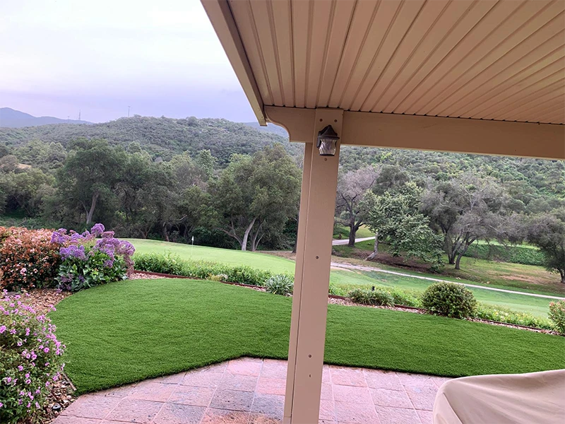 View of green lawn and trees from a covered patio with mountains in the background