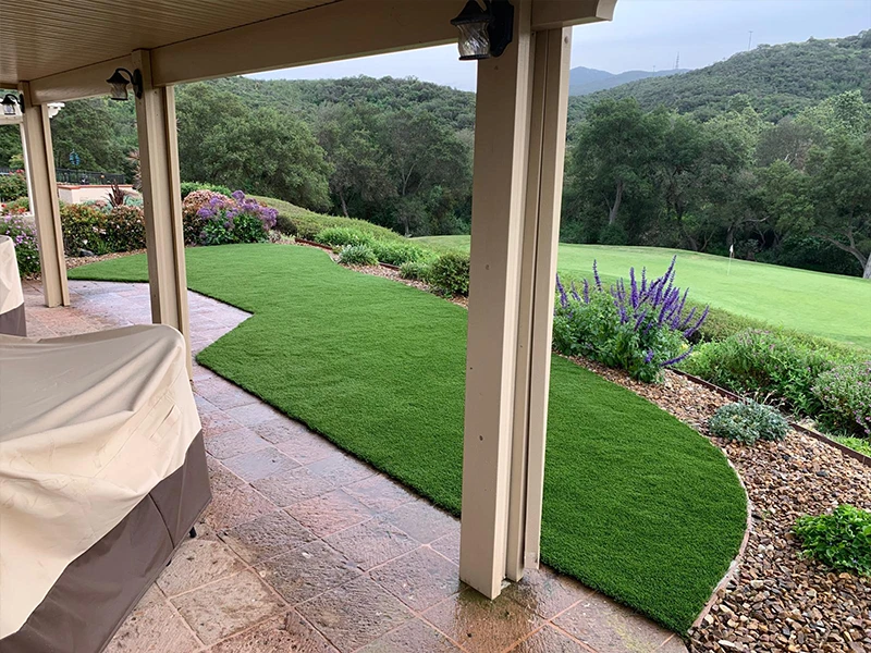 View from a covered patio showing grass and landscaped garden with trees in the background
