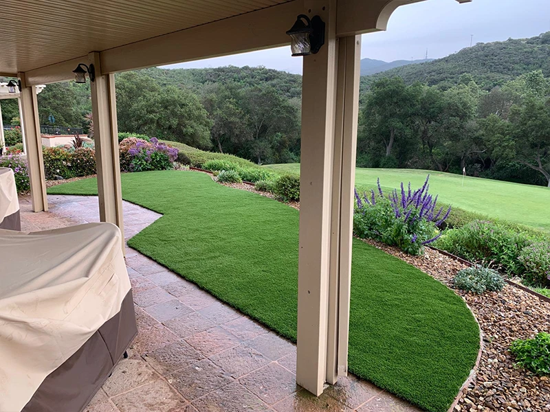 A patio view of a landscaped yard with grass, plants, and a distant hillside
